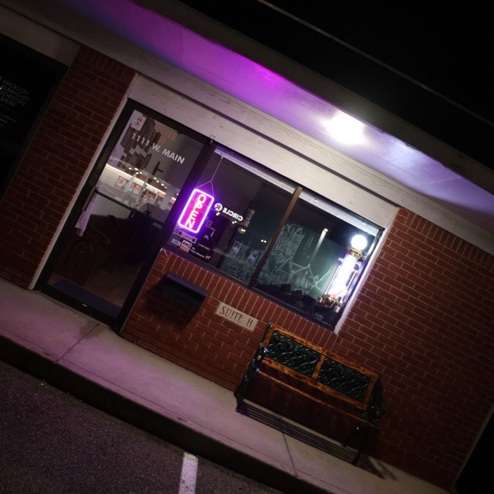 The Greenfield Barbershop storefront on West Main at night with the neon Open sign lit